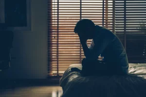 Mann sitzt traurig in dunklem Zimmer - Titelbild Hanfama Magazinbeitrag: Kann CBD gegen Depressionen helfen?
